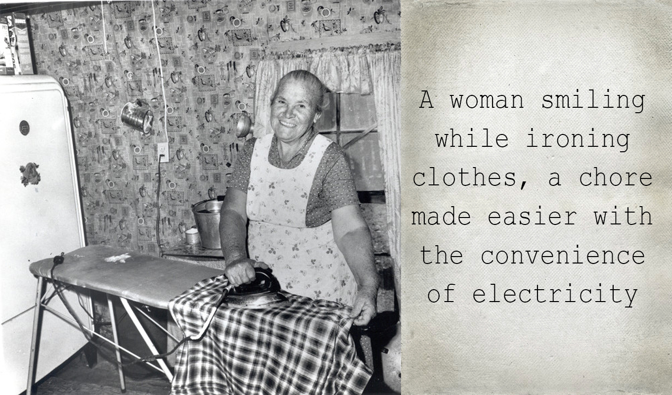 A woman smiling while ironing clothes, a chore made easier with the convenience of electricity