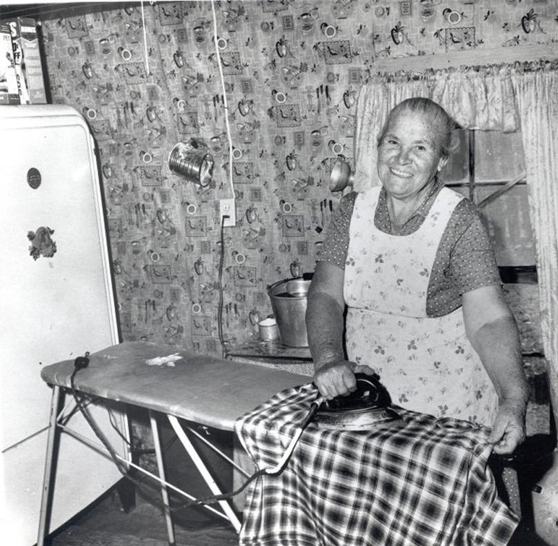 Older woman smiling while she irons after being set up with electricity. Photo Source: "The Next Greatest Thing" published by NRECA