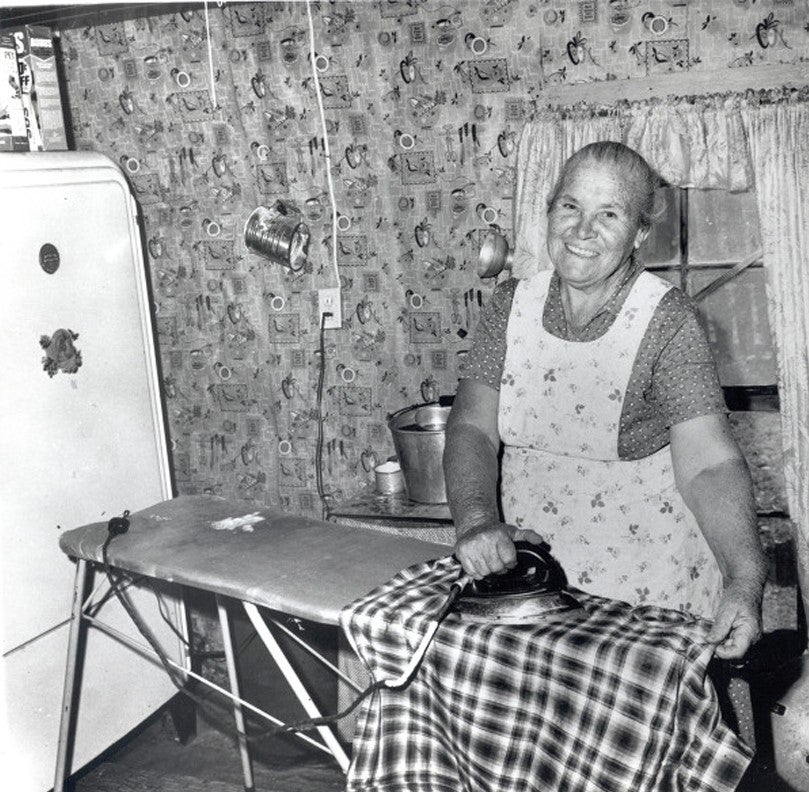 Older woman smiling while she irons after being set up with electricity. Photo Source: "The Next Greatest Thing" published by NRECA