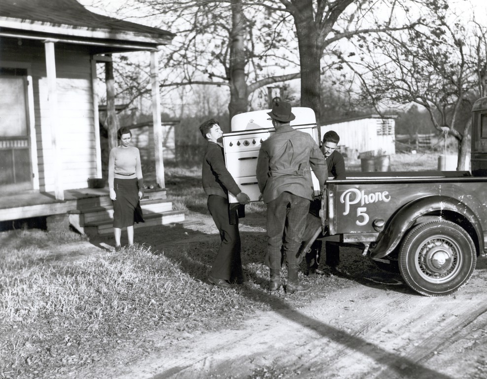Three men unload a new stove for a rural woman.  Source: The Next Greatest Thing, published by NRECA