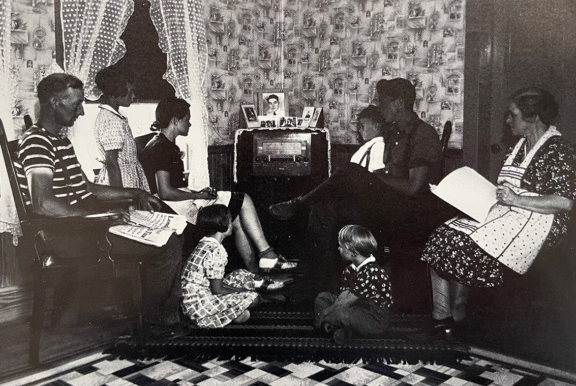 A rural family gathers around the radio in their living room.
