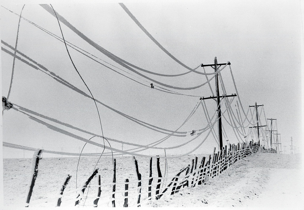 Black-and-white photo of power lines covered in ice, stretching into the distance over a snow covered landscape. Source: “The Next Greatest Thing,” published by NRECA