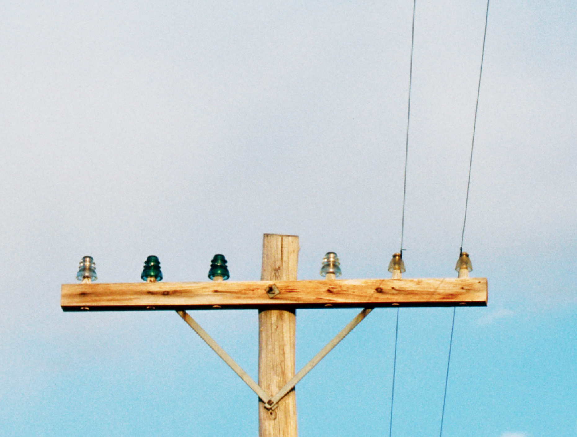 An image of a utility pole top with glass insulators. Many glass insulators were threadless and held in place with either tar or glue. Most have since been replaced by sturdier insulators made from porcelain or polymer composites.