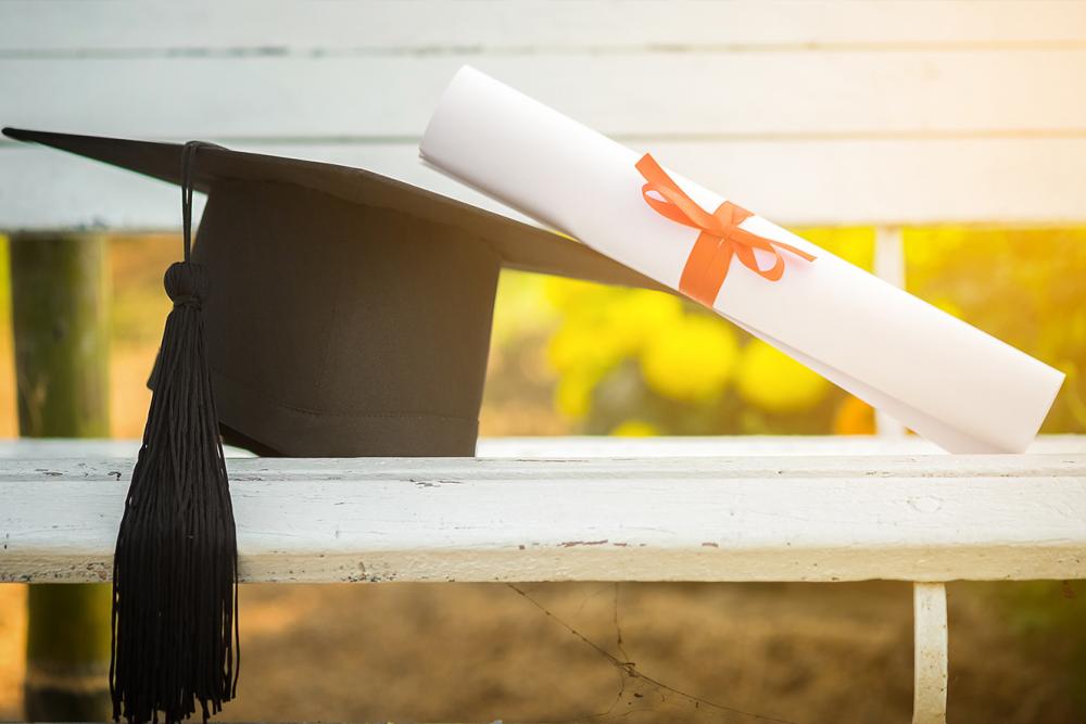 Graduation cap laying on a bench with a diploma leaning on it