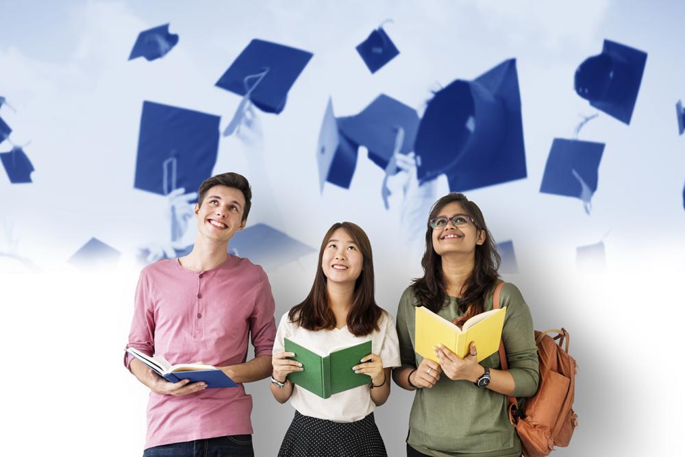 Students holding books looking up, with the wall behind them decorated with images of graduation caps flying through the air