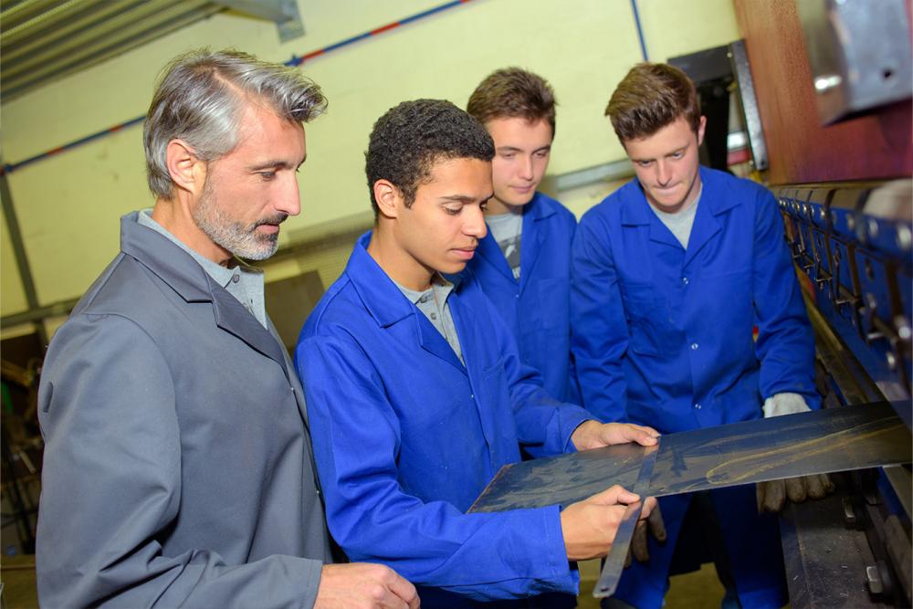 Trade school students performing hands-on work with their instructor watching